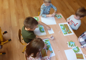 Dzieci przyklejają wycięte puzzle na kartkę papieru.